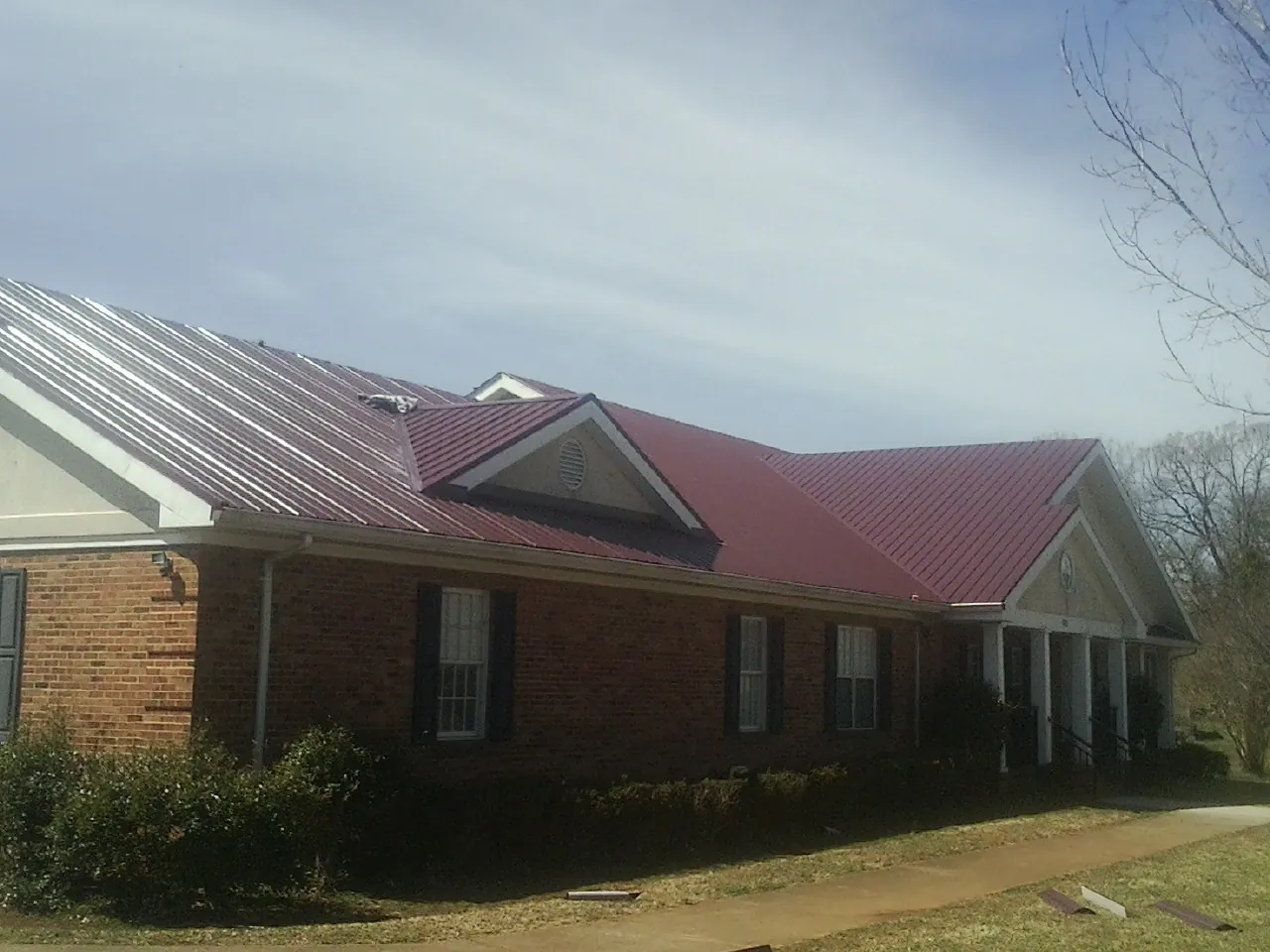 Red metal roof with gabled entries on a long brick building, from a Hail Damage Roof Repair job in Stevensville